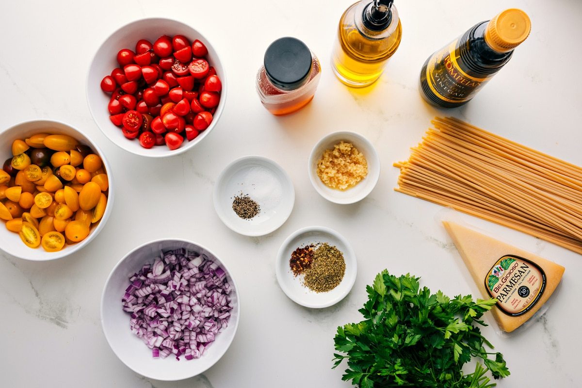 All the ingredients in this recipe prepped out for straightforward assembly including the tomatoes, onion, seasonings, oil, honey, vinegar, parmesan, pasta, and parsley.