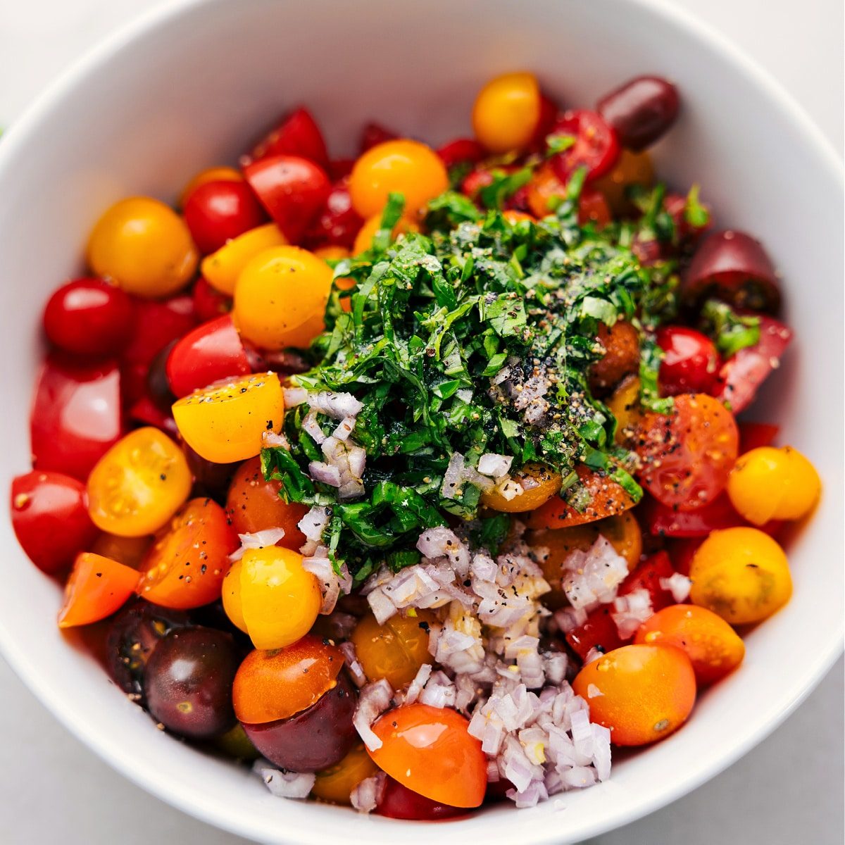 All the ingredients in this cherry tomato salad recipe in a bowl ready to be tossed together.