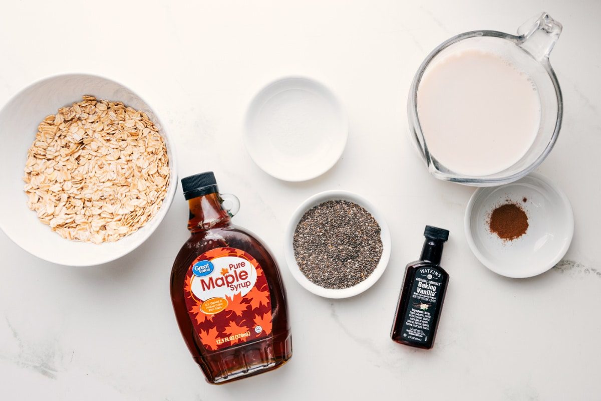 All the ingredients in this recipe prepped out for straightforward assembly including the oats, mape syrup, milk, cinnamon, chia seeds, vanilla, an salt.
