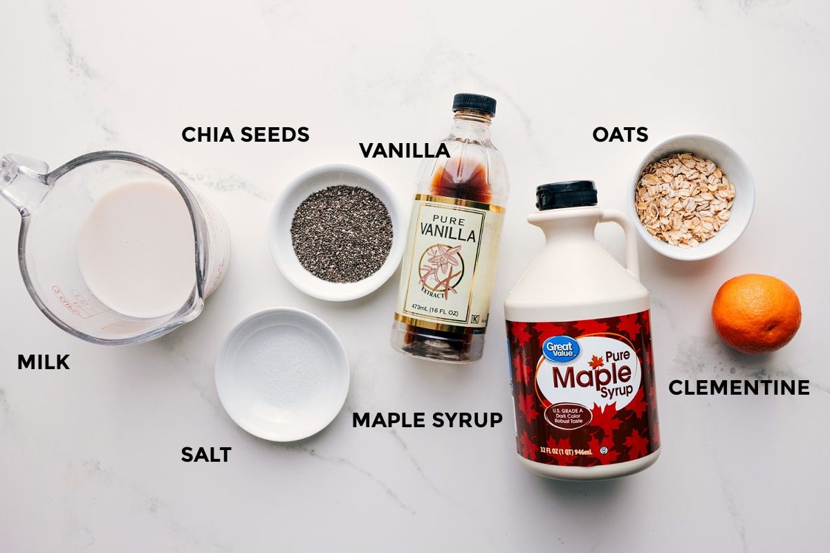 All the ingredients in this recipe prepped out for straightforward assembly including the milk, chia seeds, salt, maple syrup, vanilla, oats, and clementine.