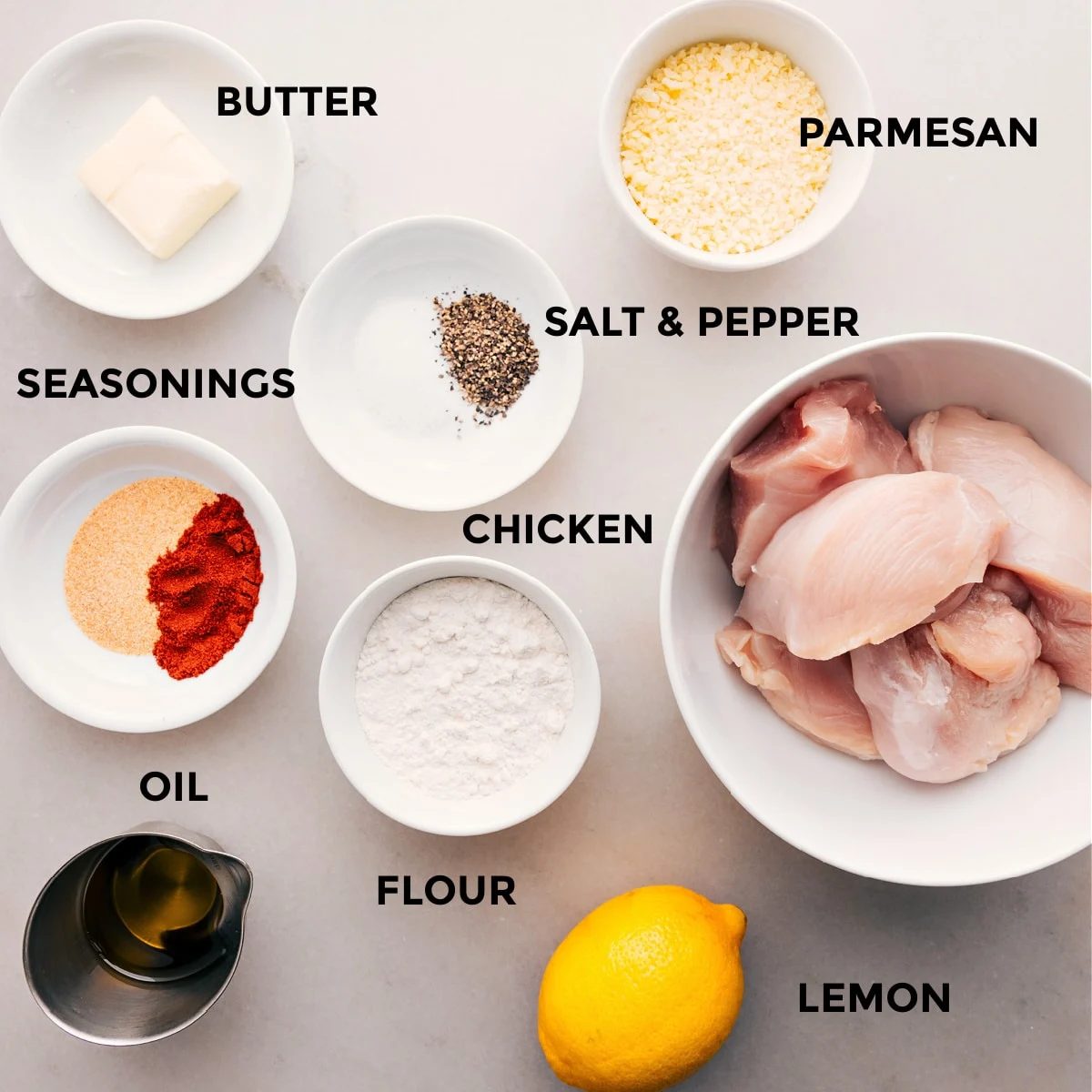 All the ingredients for this recipe are prepped and ready for straightforward assembly: butter, parmesan, seasonings, meat, flour, lemon, and oil.