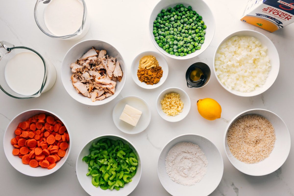 All the ingredients in this recipe prepped out for straightforward assembly including the chicken, rice, curry powder, cream, broth, veggies, butter, oil, and lemon.