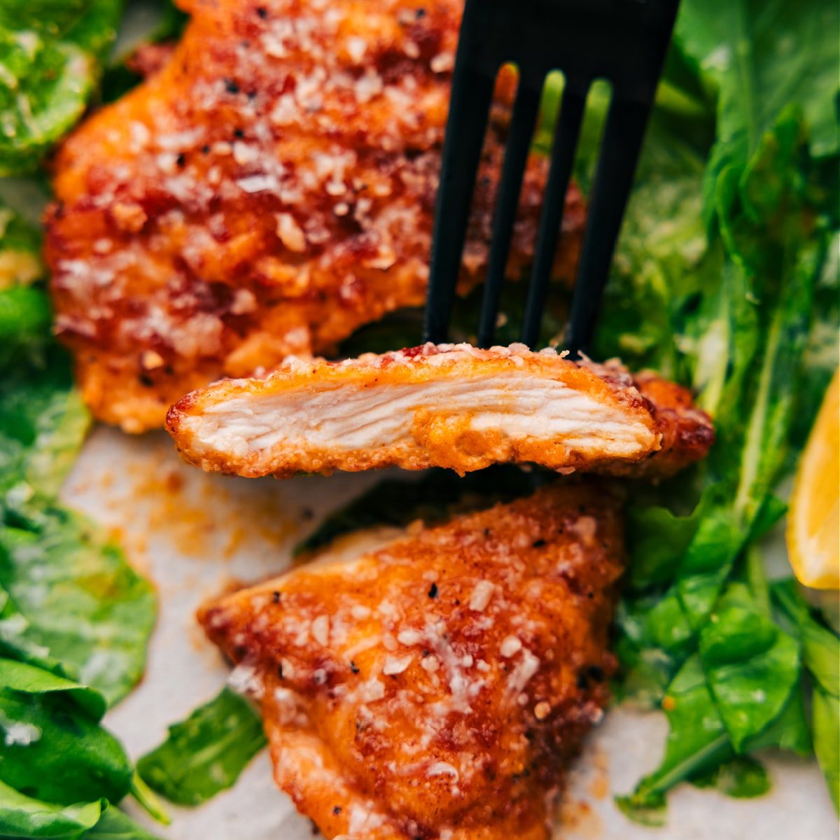 A slice of the chicken cutlet is held up with a spoon, showing its tender and evenly cooked inside.