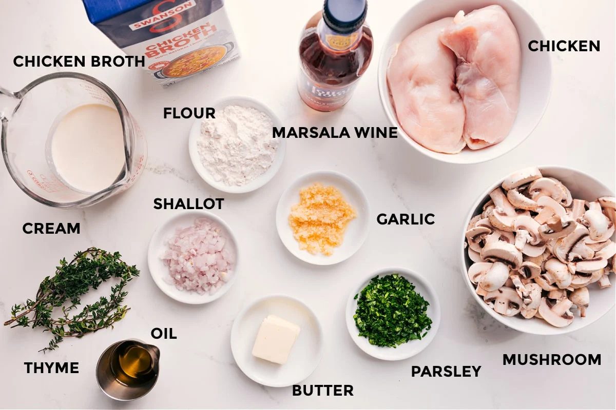 All the ingredients in this recipe prepped out for straightforward assembly including the cream, chicken broth, thyme, oil, shallot, flour, wine, butter, garlic, parsley, mushrooms, and chicken.