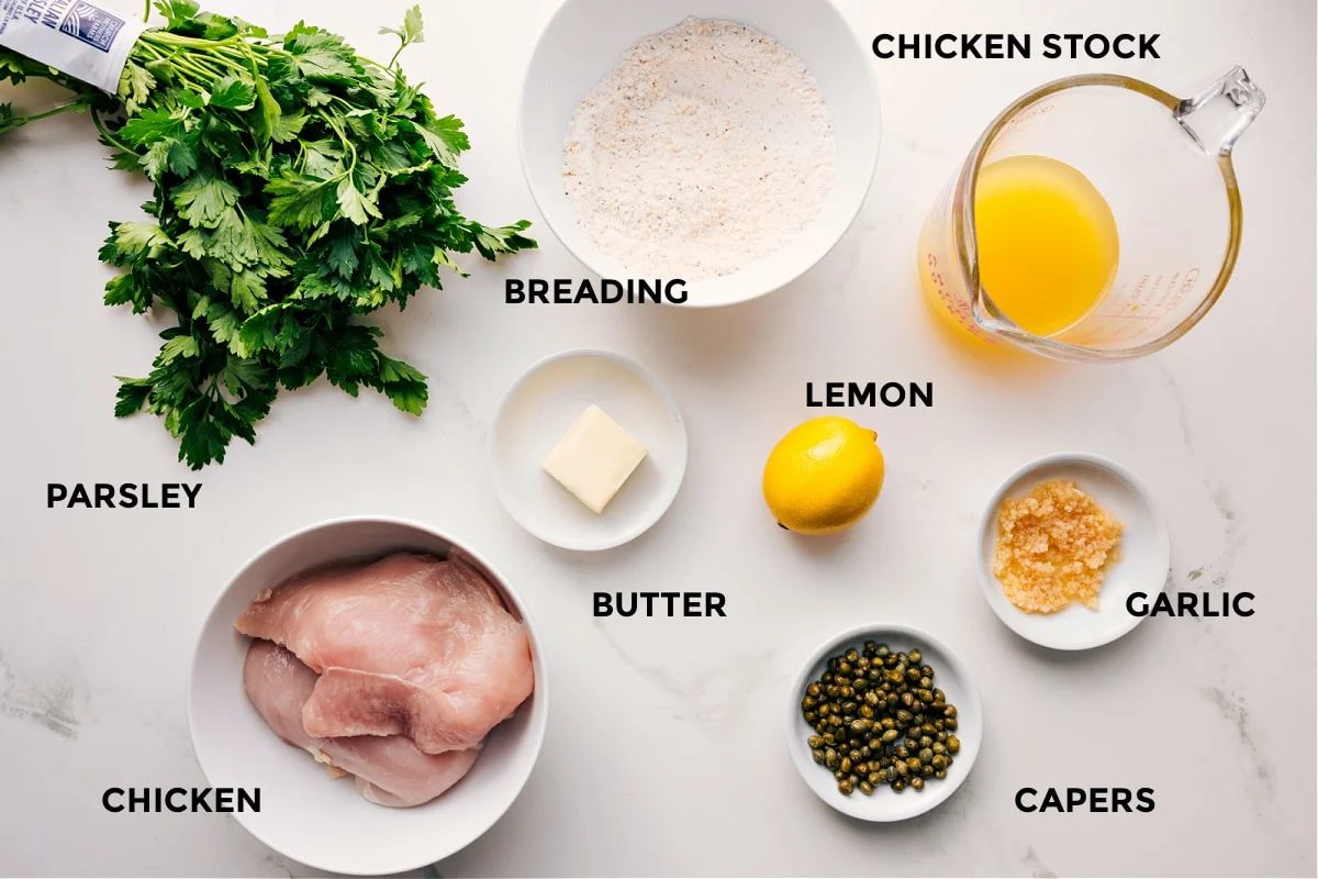 Ingredients in this recipe prepped for straightforward assembly including parsley, chicken, breading, butter, lemon, capers, garlic, and stock.