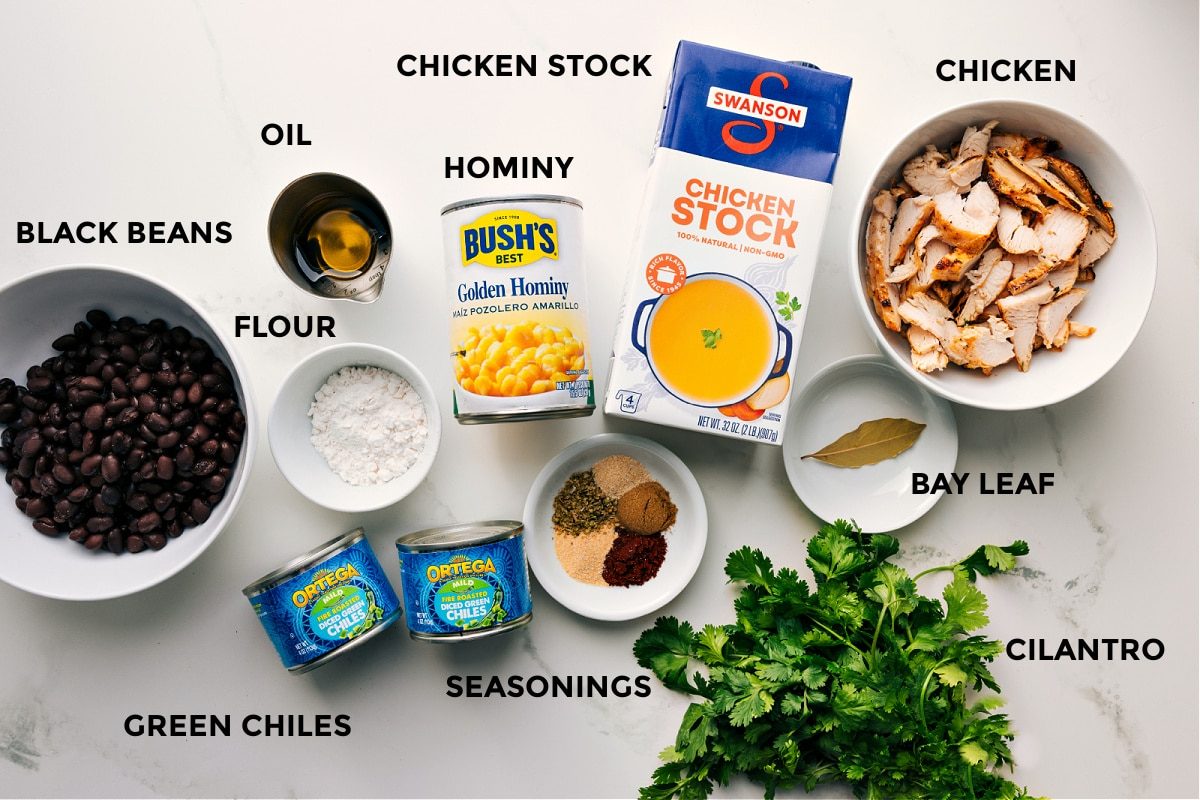 Prepped ingredients for this recipe laid out for straightforward assembly, including black beans, flour, green chiles, seasonings, oil, hominy, stock, bay leaf, chicken, and cilantro.
