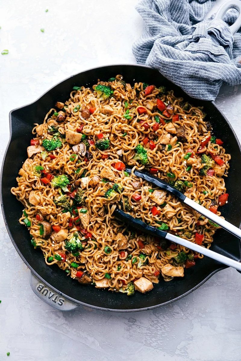 Use tongs to hold some of the noodles while cooking chicken ramen in a skillet.
