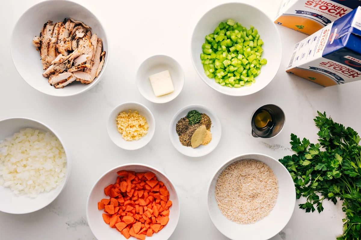 All the ingredients in this recipe prepped out for straightforward assembly including the chicken, veggies, garlic, seasonings, butter, oil, stock, parsley, and rice.
