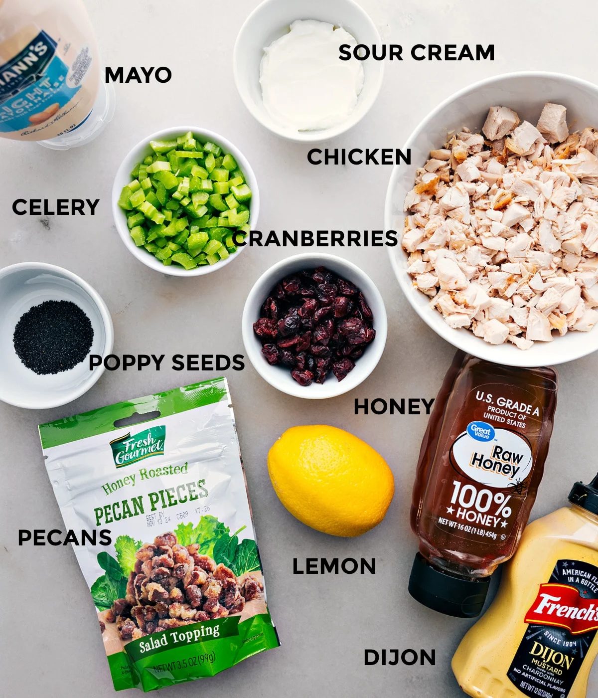 All the ingredients in this recipe including meat, sour cream, mayo, celery, cranberries, poppy seeds, lemon, dijon, pecans, and honey prepped out for straightforward assembly.