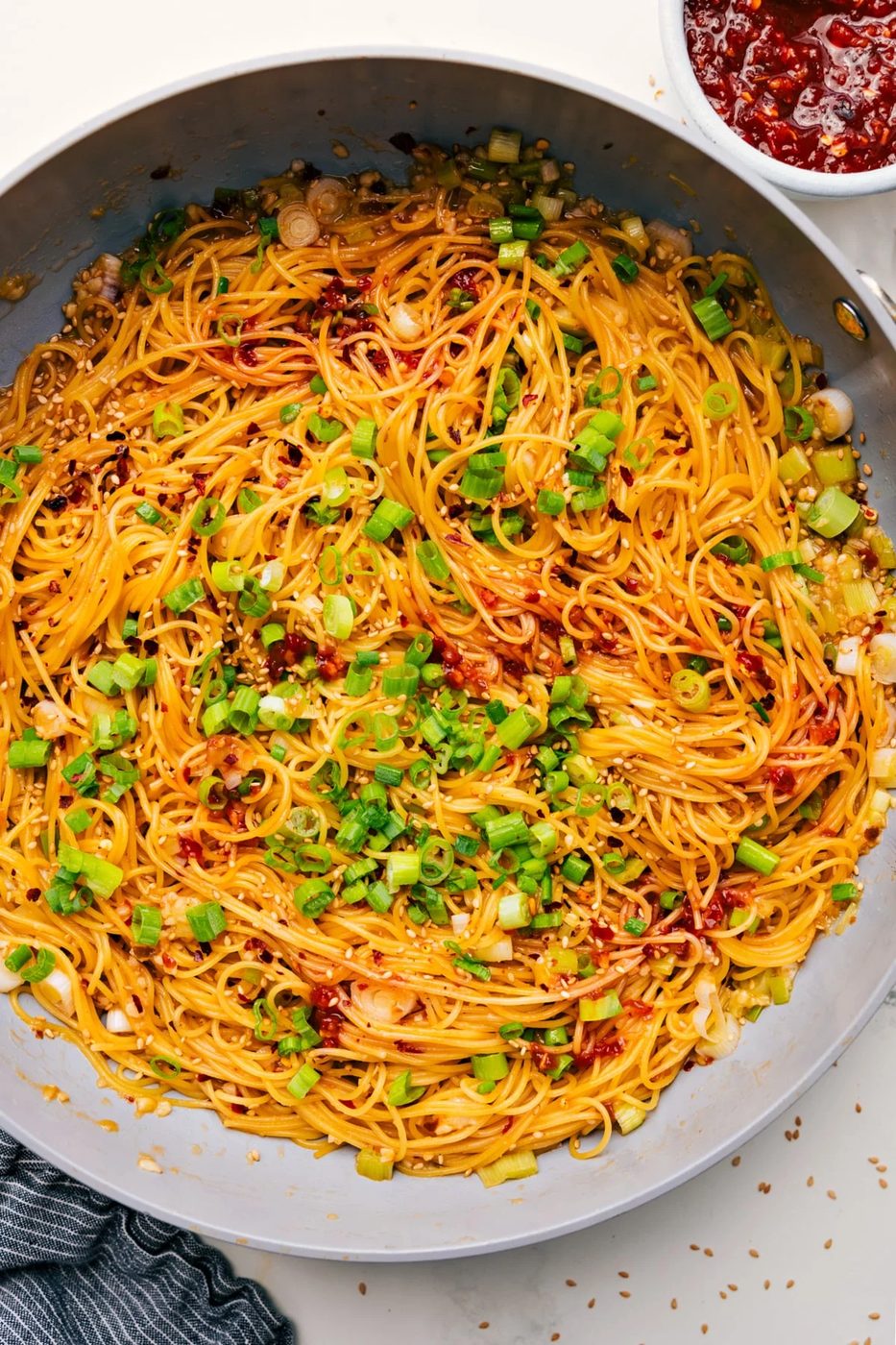 Chili Garlic Noodles in a skillet, garnished with green onions and sesame seeds.