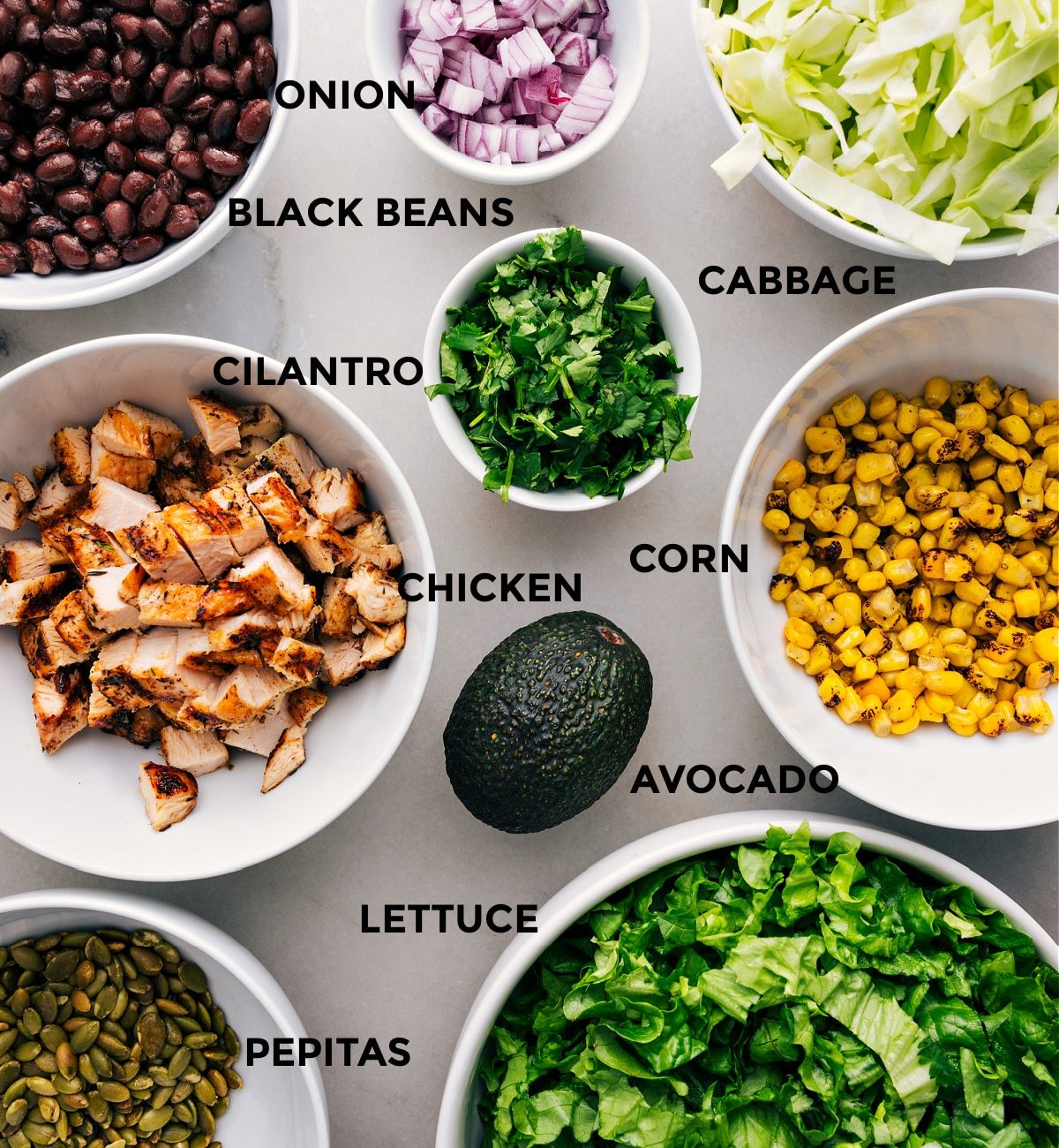 Lettuce and cabbage, pepitas, corn, black beans, avocado, chicken, cilantro, and red onion prepped out for straightforward assembly of this recipe.