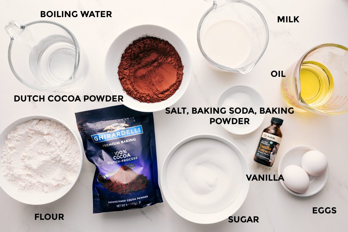 All the ingredients in this recipe prepped out for straightforward assembly including the boiling water, flour, cocoa powder, salt, baking soda, baking powder, sugar, vanilla, eggs, oil, and milk.