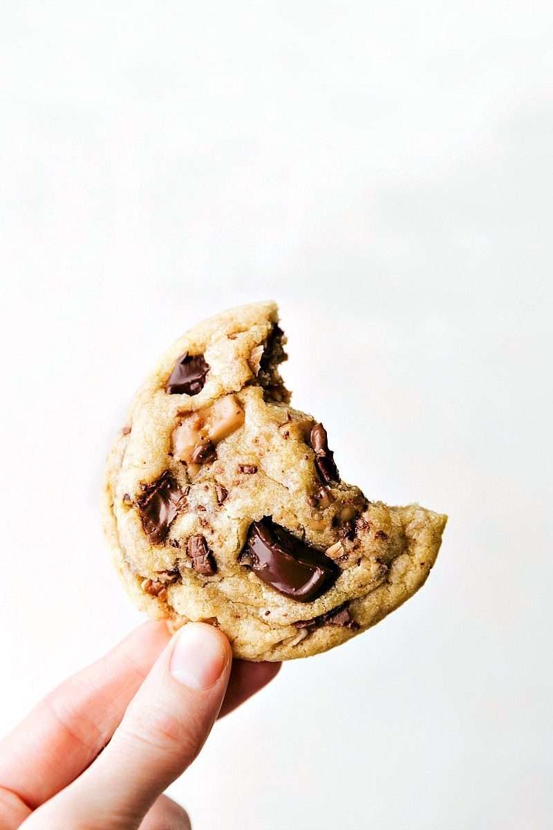 A toffee cookie being held with a bite taken out, showcasing its delightful texture.