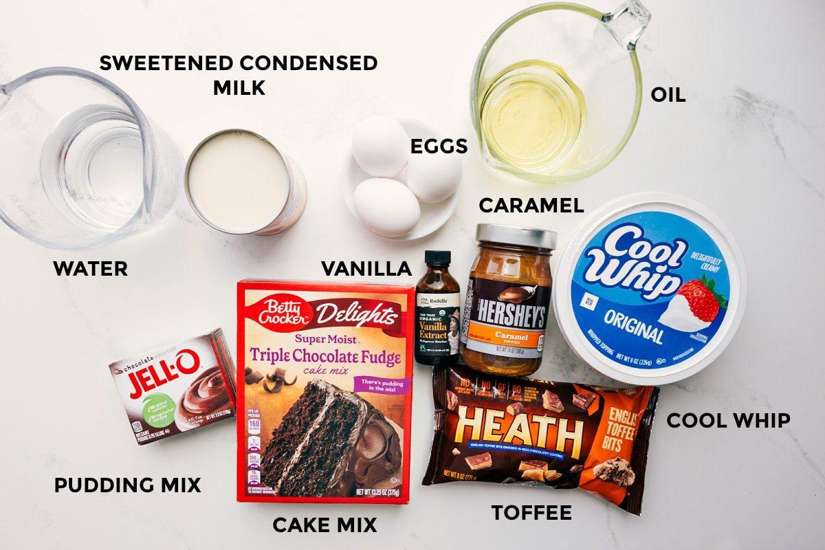 All the ingredients in this recipe prepped out for straightforward assembly including the sweetened condensed milk, water, pudding mix, cake mix, toffee, cool whip, caramel, vanilla, oil, and eggs.