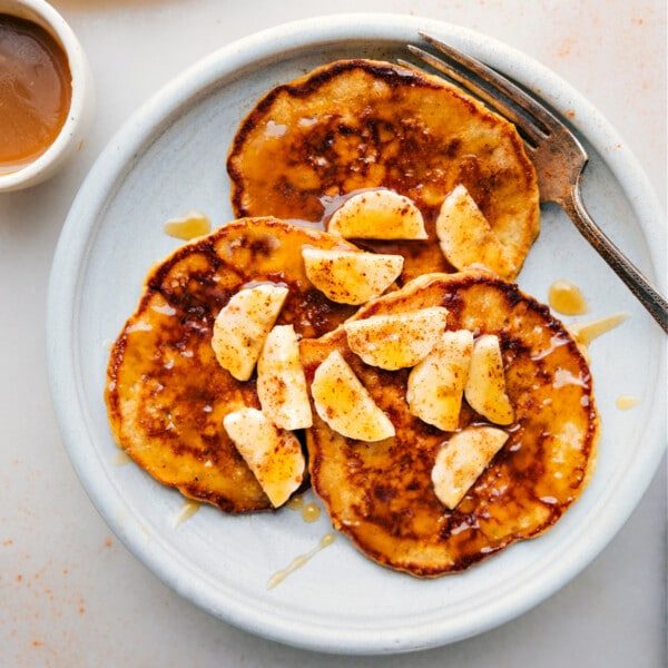 Warm banana pancakes stacked on a plate, topped with fresh banana slices and generously drizzled with syrup, creating a satisfying and inviting breakfast.