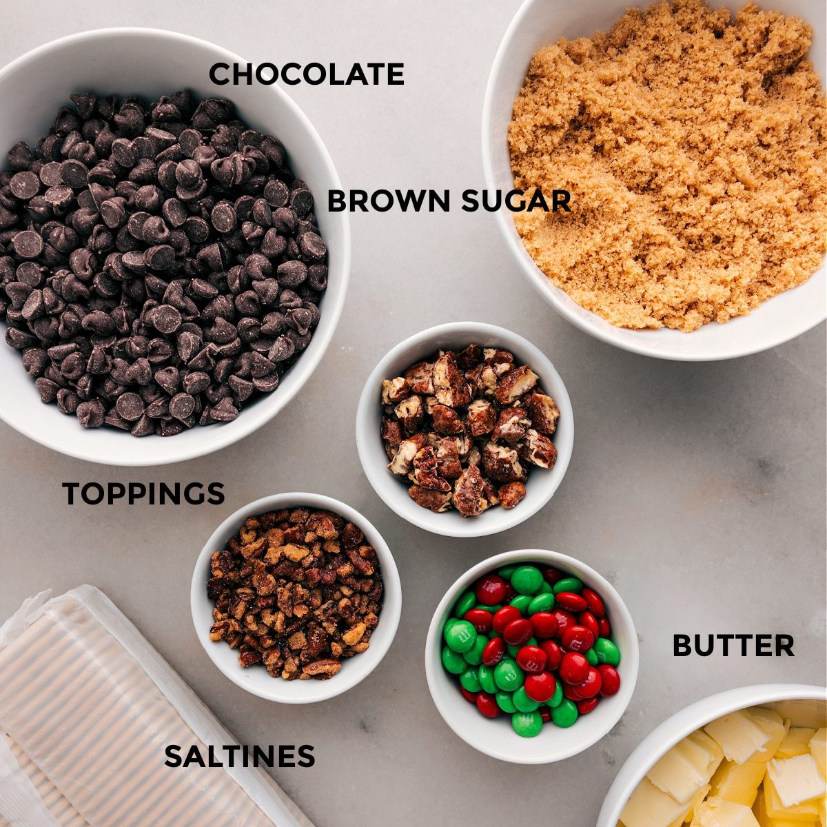 The ingredients for this recipe are prepped for straightforward assembly: chocolate, brown sugar, toppings, butter, and saltines.