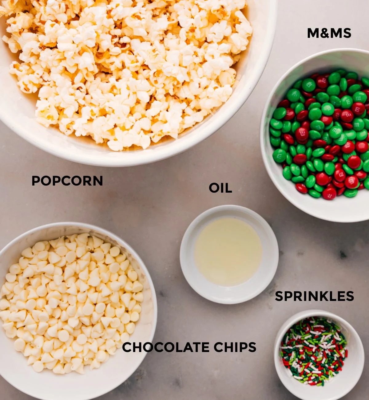 Prep all the ingredients for straightforward assembly: M&Ms, oil, sprinkles, popcorn, and white chocolate.