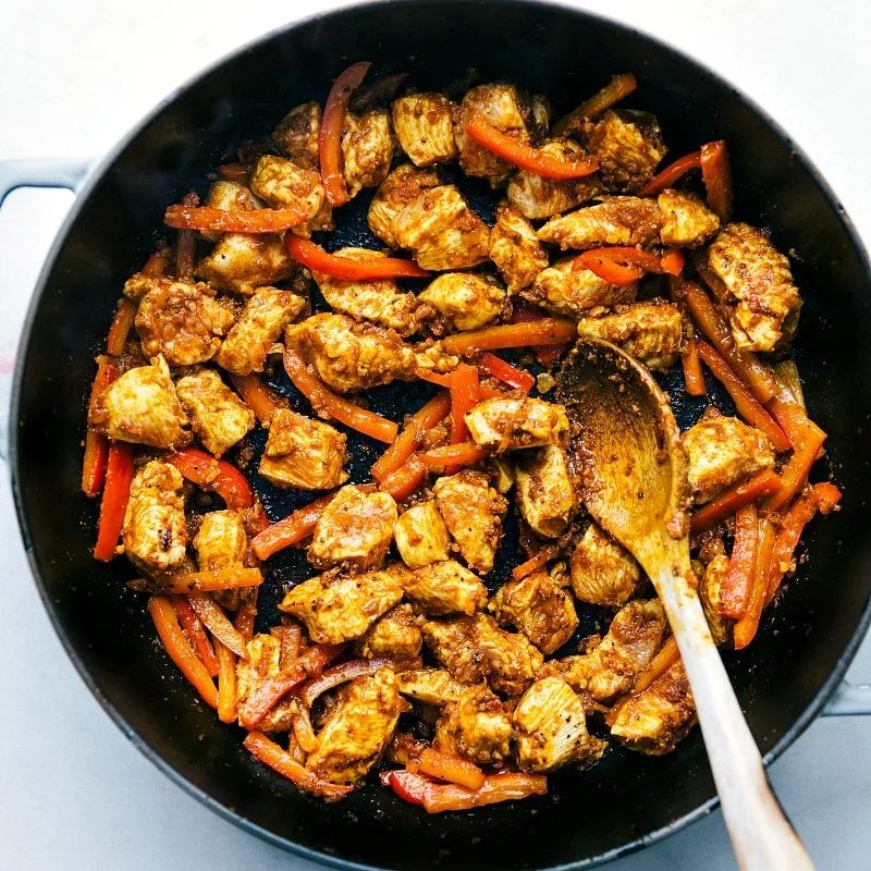 Chicken and red peppers cooking in a pan for coconut chicken curry, starting to combine with spices and flavors.