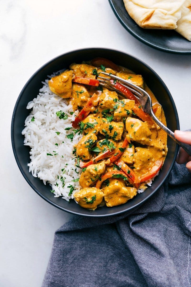 Ready-to-eat coconut curry chicken, creamy and flavorful, with a fork in it, served alongside fluffy rice and warm naan bread.