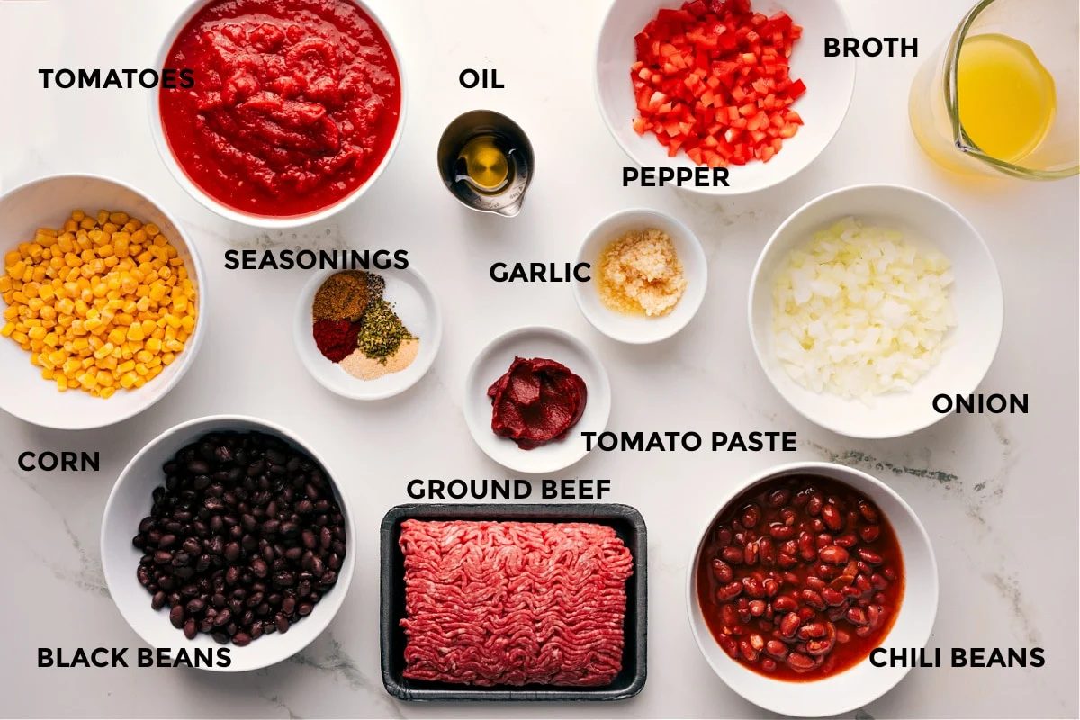 The ingredients in this recipe prepped out for straightforward assembly including the corn, black beans, tomatoes, seasonings, oil, ground beef, garlic, peppers, onions, chili beans, and broth.
