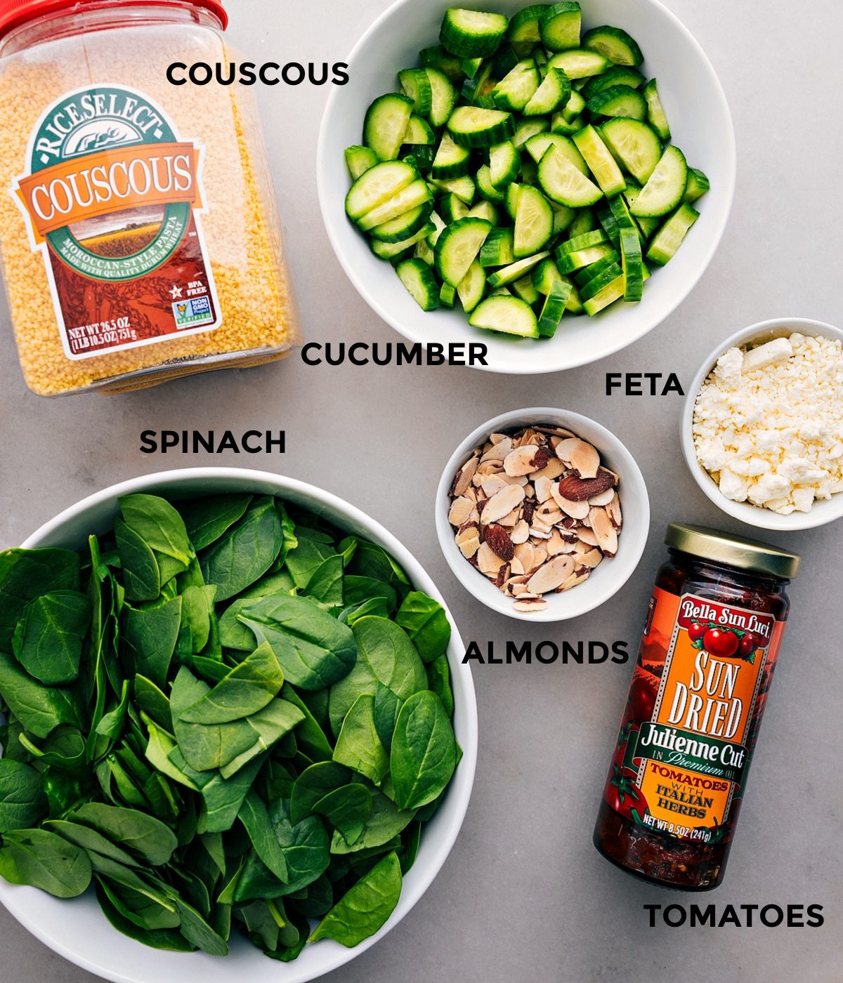 All the Couscous Mediterranean Salad ingredients prepped for straightforward assembly: cucumber, feta, almonds, tomatoes, spinach, and couscous.