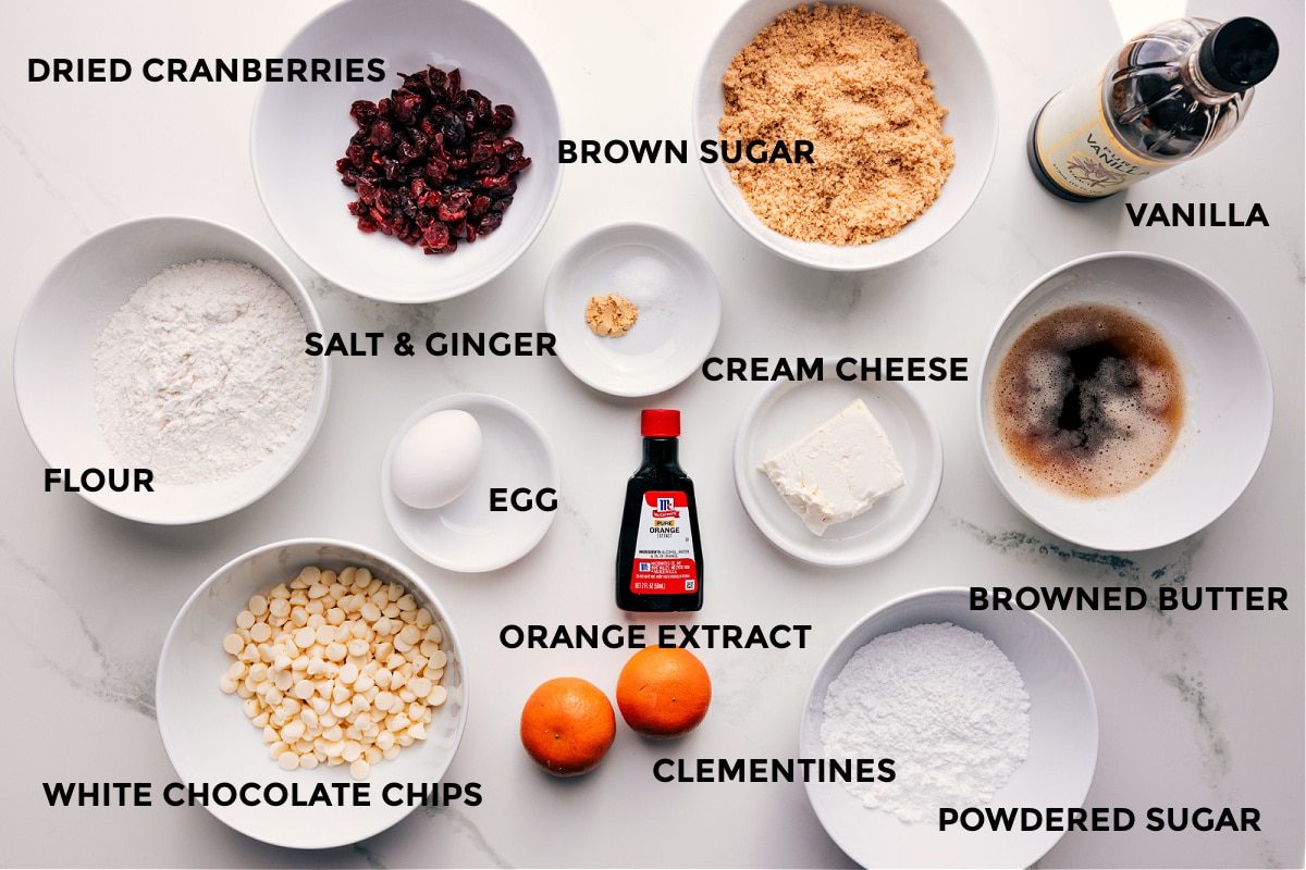 All the ingredients in this recipe prepped out for straightforward assembly including flour, cranberries, white chocolate chips, brown sugar, salt, ginger, egg, orange extract, clementines, cream cheese, powdered sugar, browned butter, and vanilla.