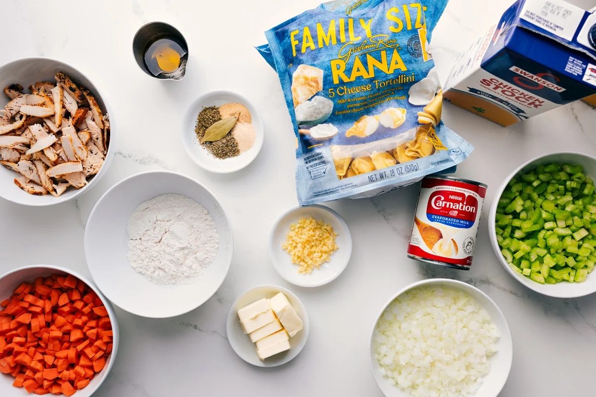 All the ingredients in this recipe prepped out for straightforward assembly including the chicken, onion, carrots, celery, butter, olive oil, flour, chicken broth, bouillon, tortellini, and evaporated milk.