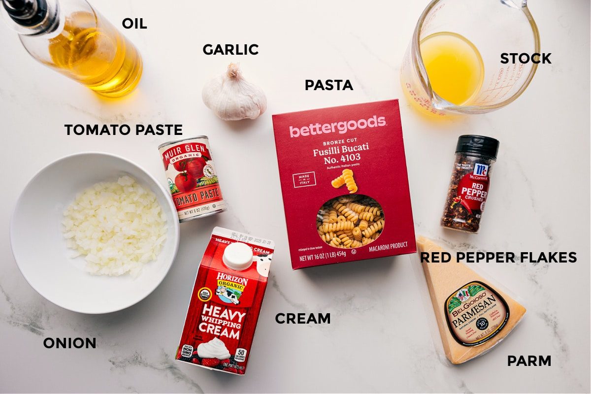 Ingredients for creamy tomato pasta prepped for straightforward assembly, including oil, garlic, onion, tomato paste, cream, pasta, stock, red pepper flakes, and Parmesan.