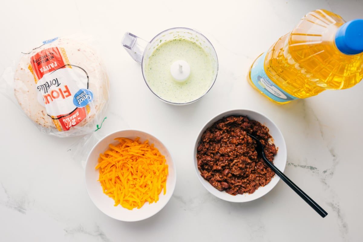 All the ingredients in this recipe prepped out for straightforward assembly including the tortillas, cheese, sauce, beef, and oil.