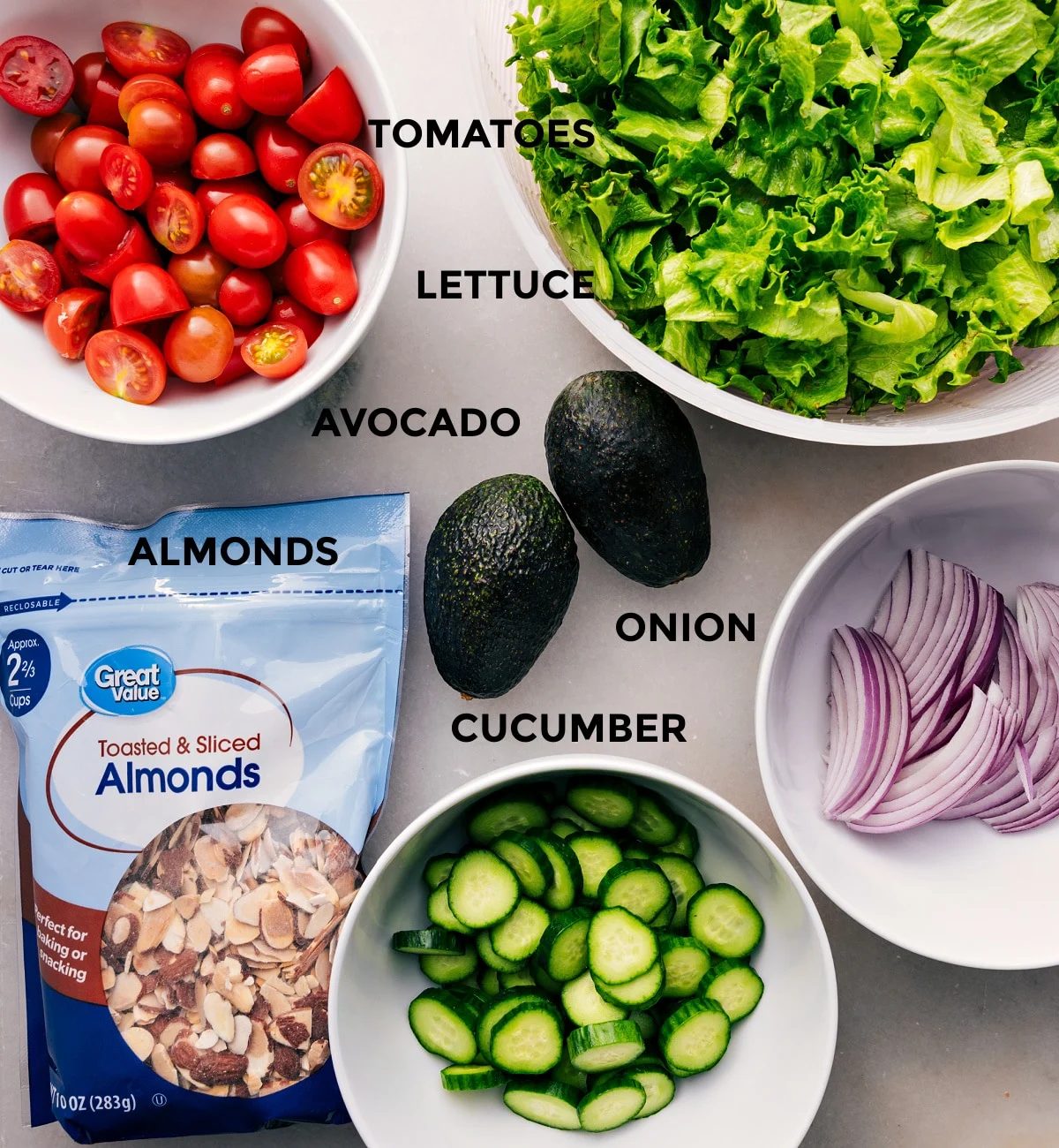 This recipe uses prepped ingredients for straightforward assembly: lettuce, tomatoes, avocado, onion, cucumber, and almonds.