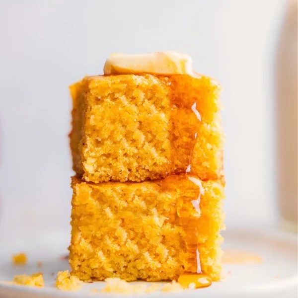 Stack of satisfying and fluffy cornbread with honey and butter on a plate.