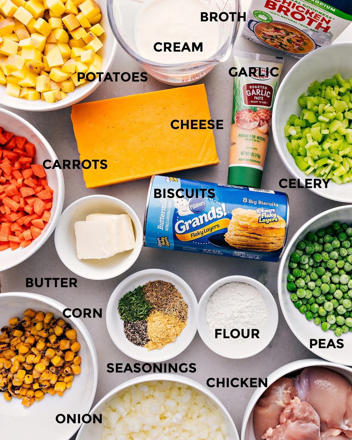 slow cooker Chicken Pot Pie ingredients are prepped for straightforward assembly, including cheese, celery, veggies, biscuits, flour, meat, broth, and cream.