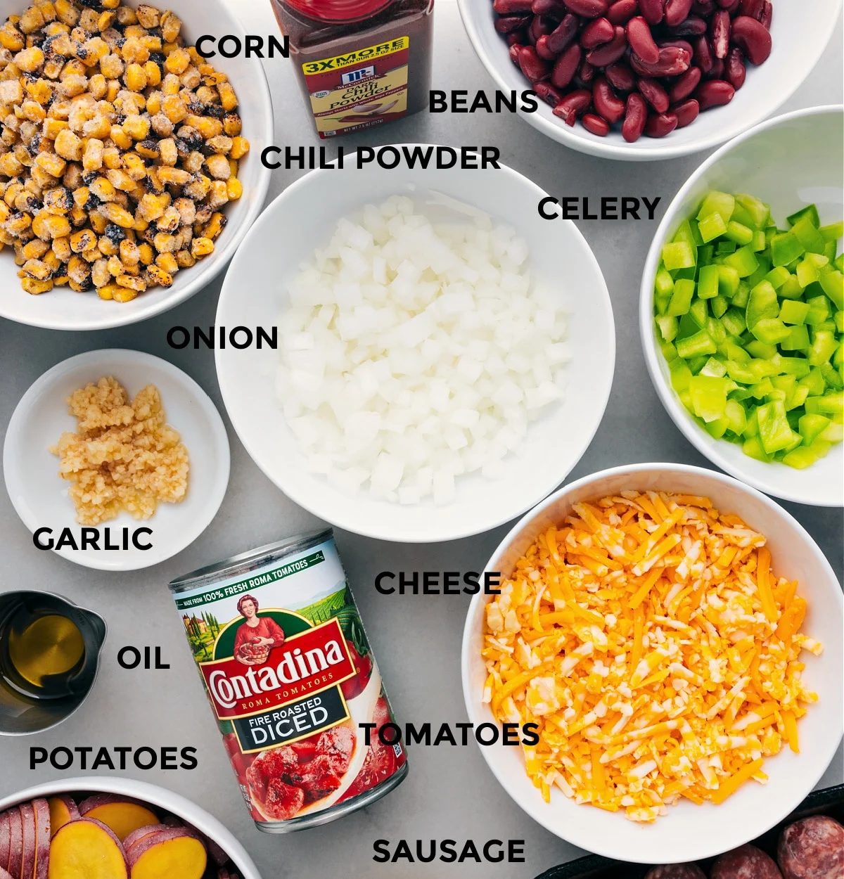 All the ingredients in this recipe are prepped for straightforward assembly, including the veggies, cheese, tomatoes, potatoes, oil, corn, beans, and seasonings.