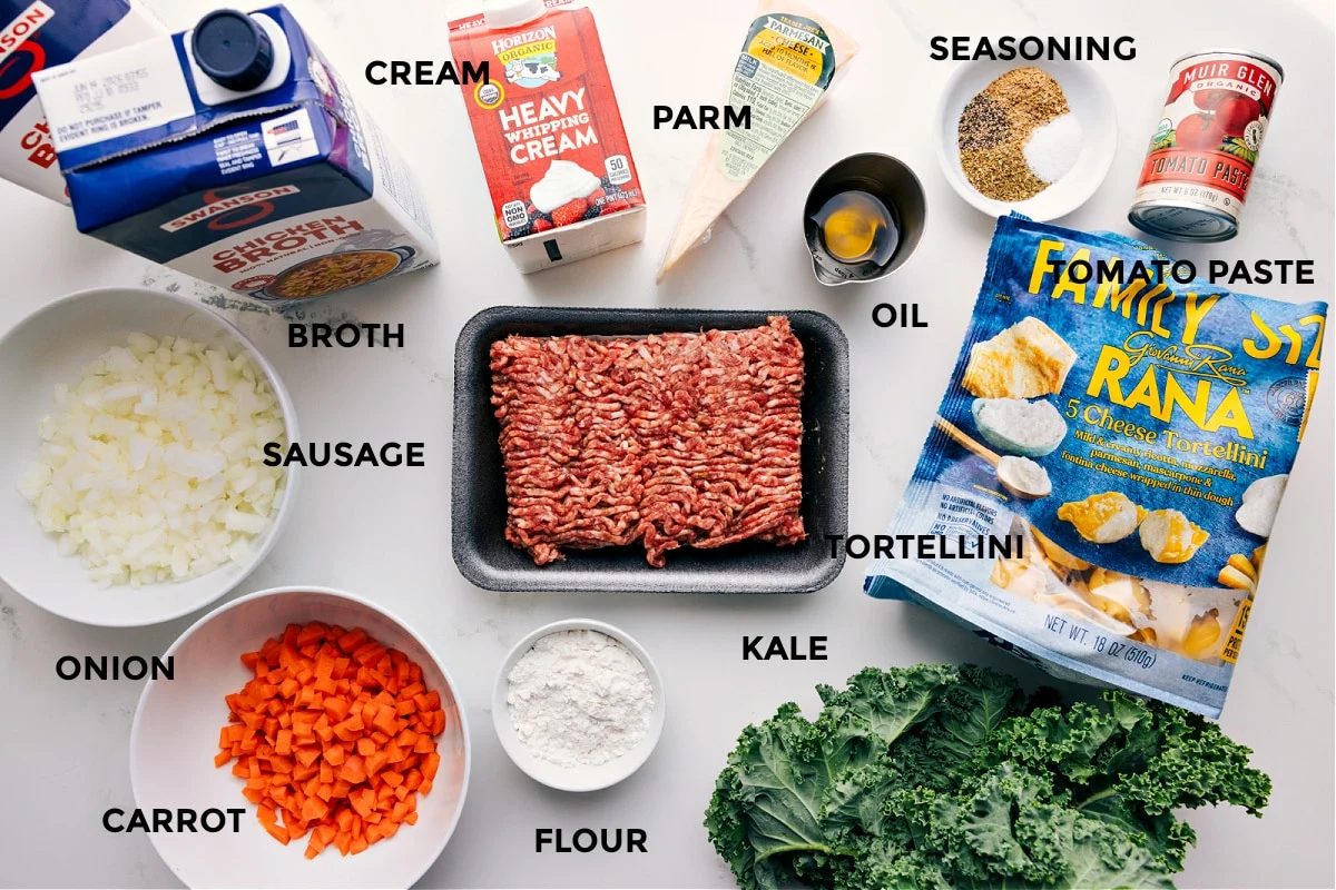 All the ingredients prepped for straightforward assembly, including broth, sausage, onion, carrot, cream, flour, Parmesan, oil, tortellini, kale, seasonings, and tomato paste.