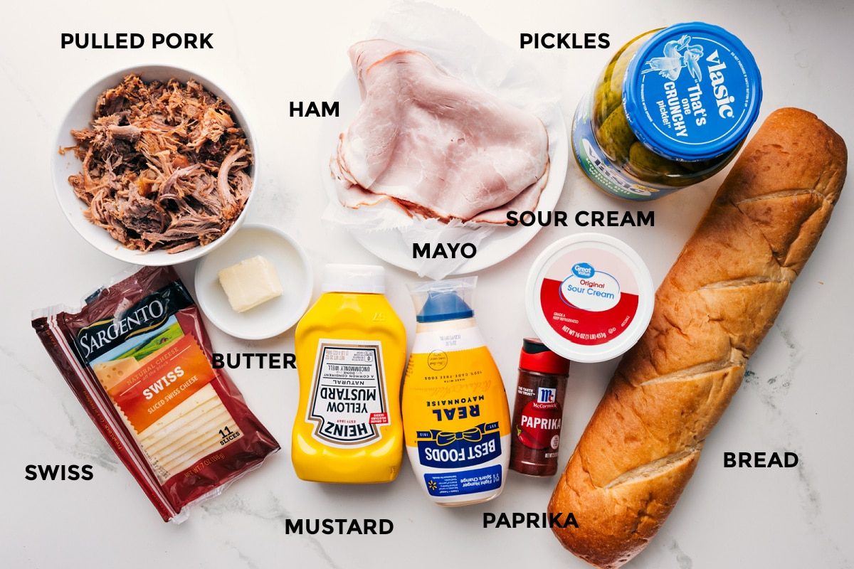 Ingredients in this recipe prepped out for straightforward assembly including the pulled pork, swiss, butter, ham, mustard, paprika, sour cream, bread, and pickles.
