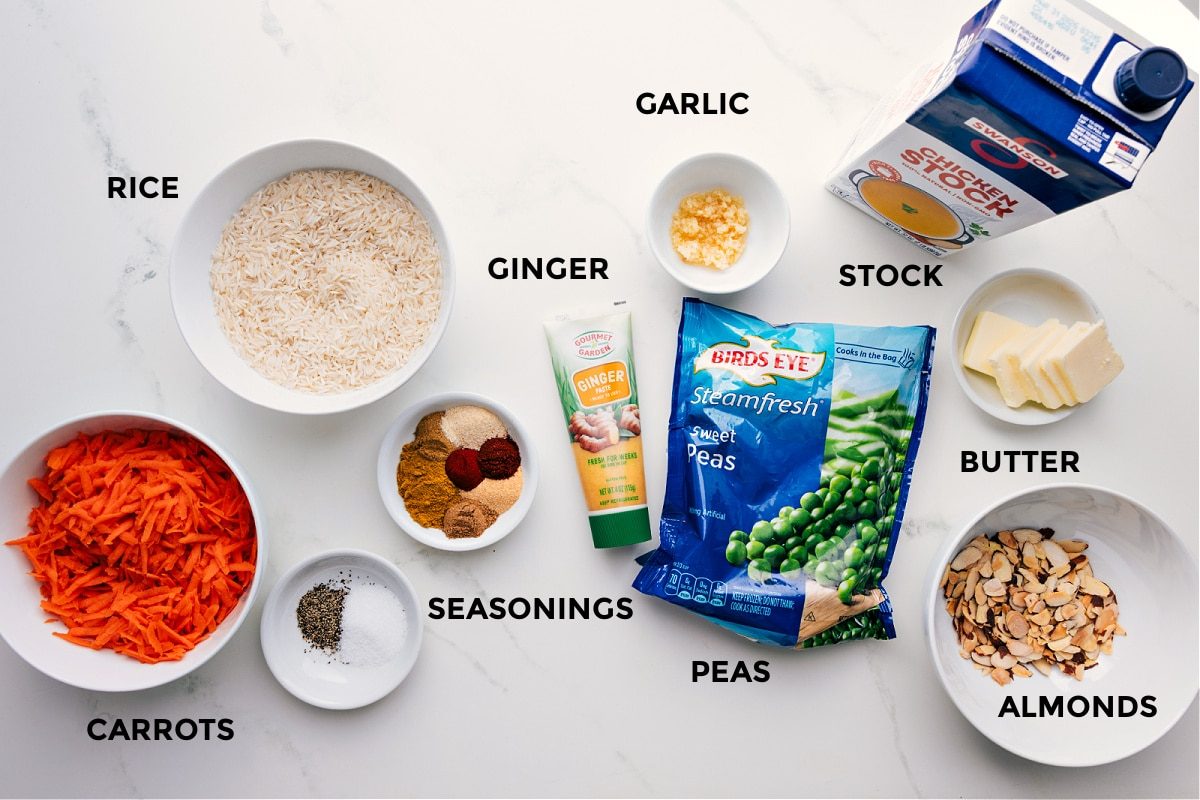 All the ingredients in this recipe prepped out for straightforward assembly including the carrots, rice, seasonings, ginger, garlic, peas, stock, butter, and almonds.
