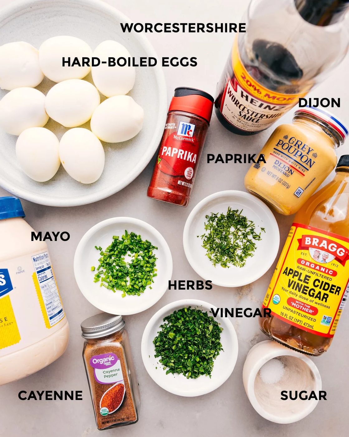 All the ingredients for this recipe are prepped and ready for straightforward assembly: eggs, Dijon, paprika, vinegar, herbs, mayo, seasonings, and sugar.