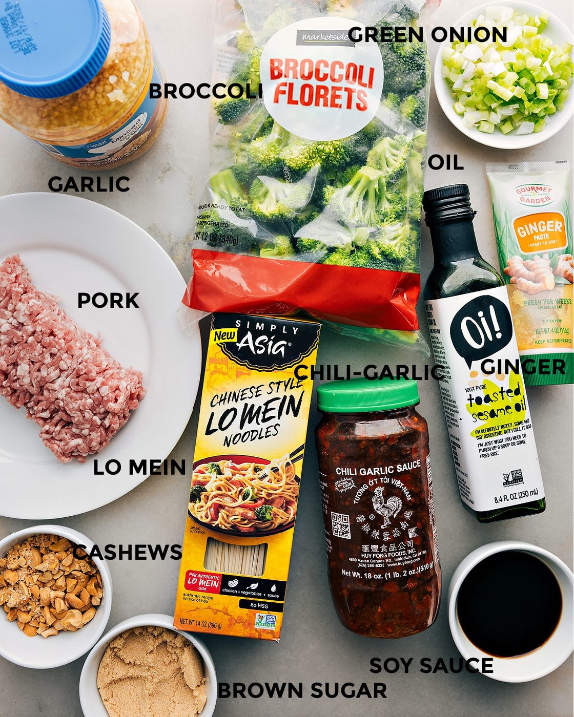 All the ingredients in this recipe including pork, broccoli, green onions, noodles, chili garlic sauce, ginger, soy sauce, brown sugar, cashews, and garlic prepped out for straightforward assembly.