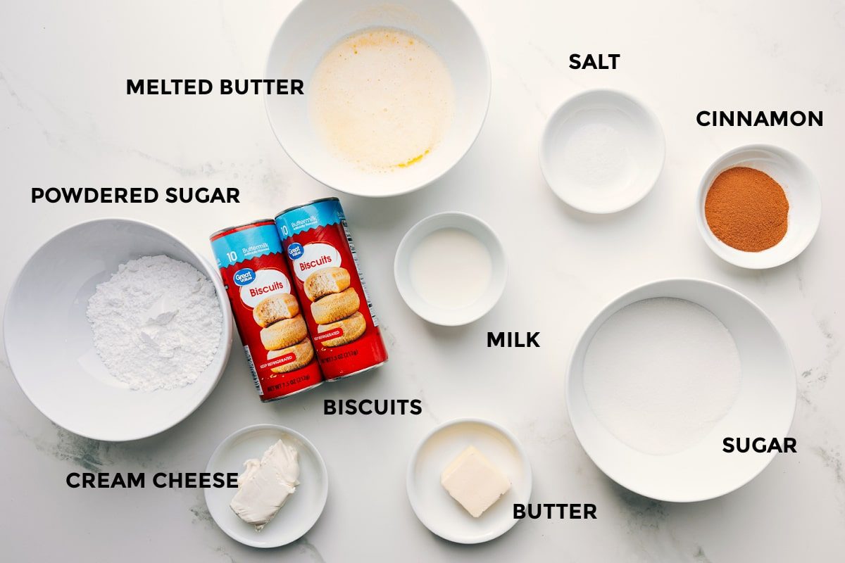 All the ingredients in this recipe prepped out for straightforward assembly including the powdered sugar, cream cheese, melted butter, biscuits, milk, butter, salt, cinnamon, and sugar.