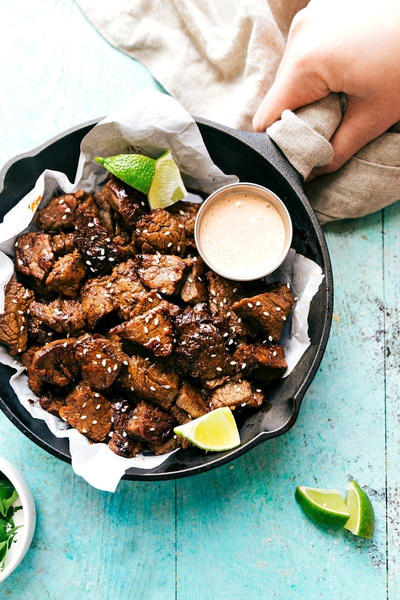 Overhead view of straightforward Asian Steak Bites in a skillet along with a small bowl of dipping sauce.