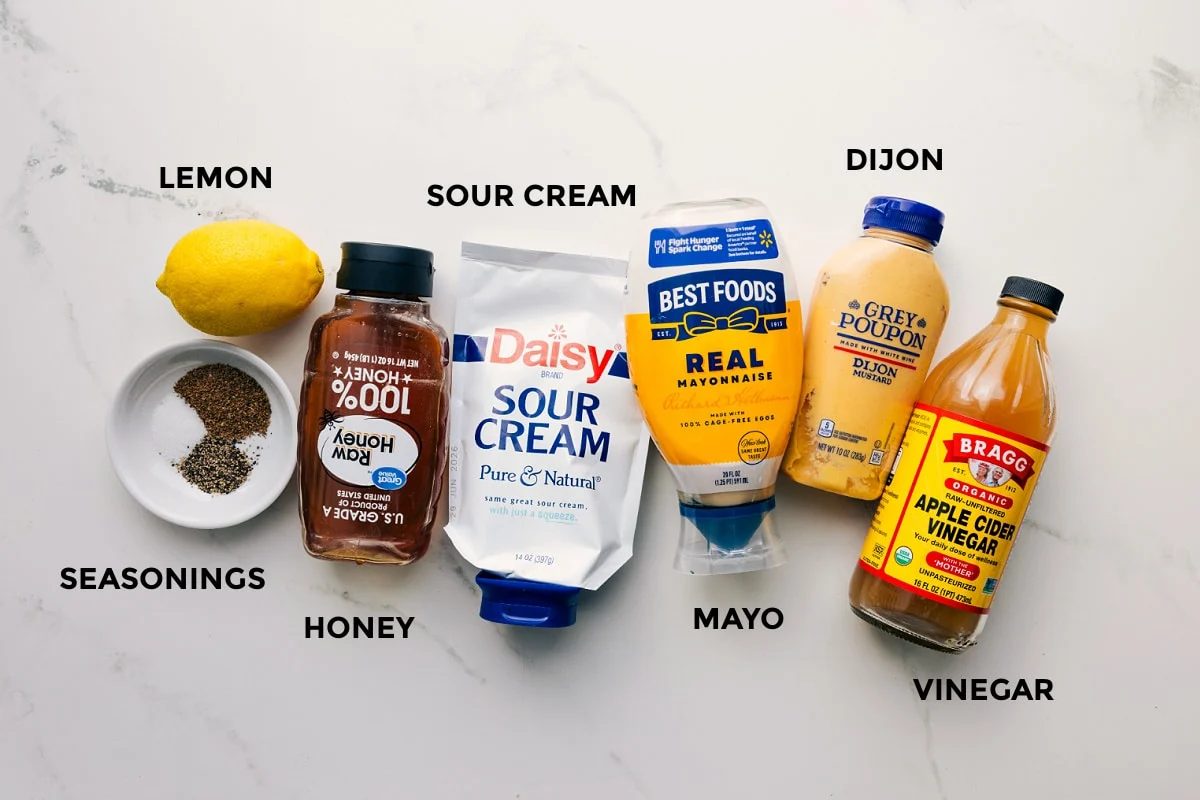 Ingredients for the straightforward Coleslaw Recipe dressing prepped for straightforward assembly, including lemon, seasonings, honey, sour cream, mayo, Dijon, and vinegar.