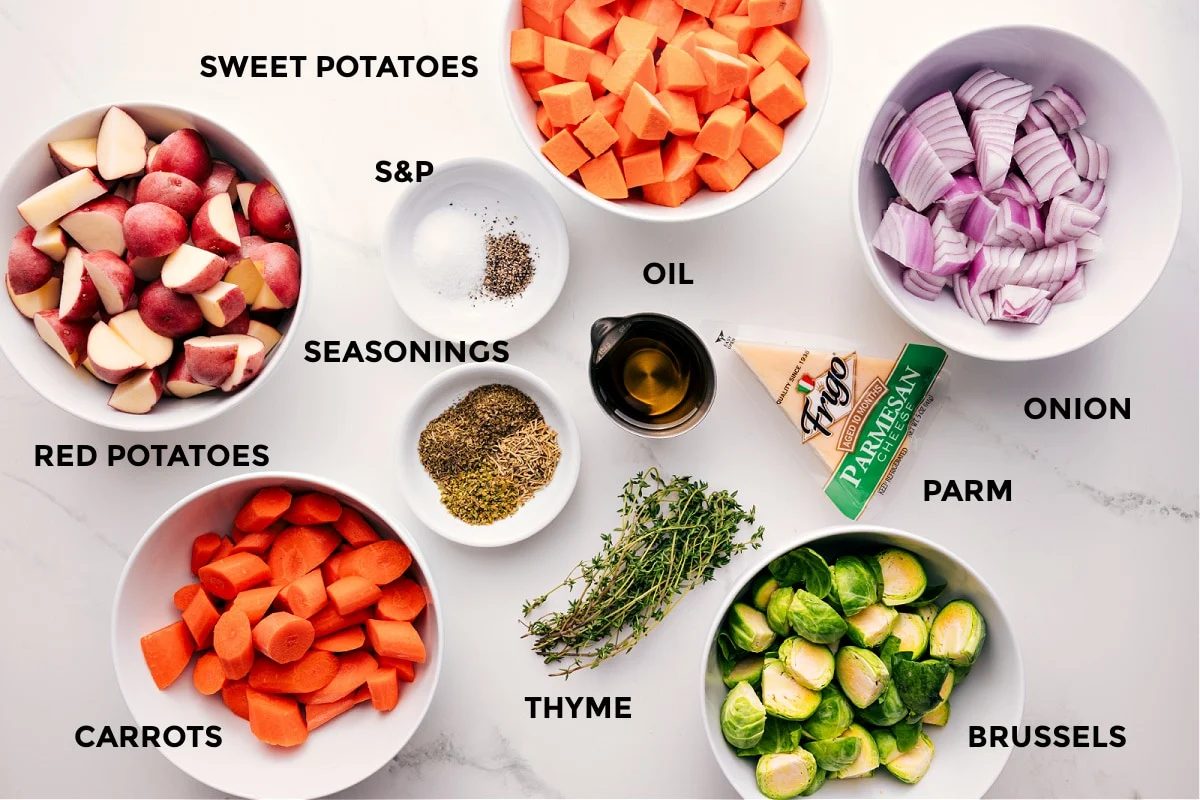 All the ingredients in this recipe prepped out for straightforward assembly including the potatoes, carrots, sweet potatoes, seasonings, oil, thyme, Brussels, parmesan, and onion,