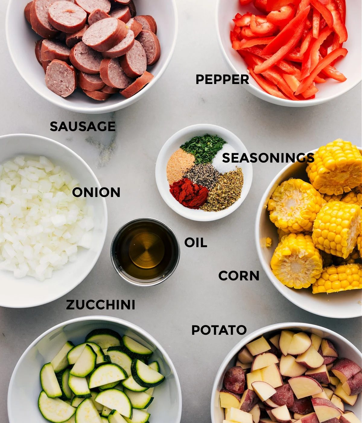 All the ingredients in this recipe including sausage, pepper, onion, seasoning, corn, zucchini, potato, and oil prepped out for straightforward assembly.