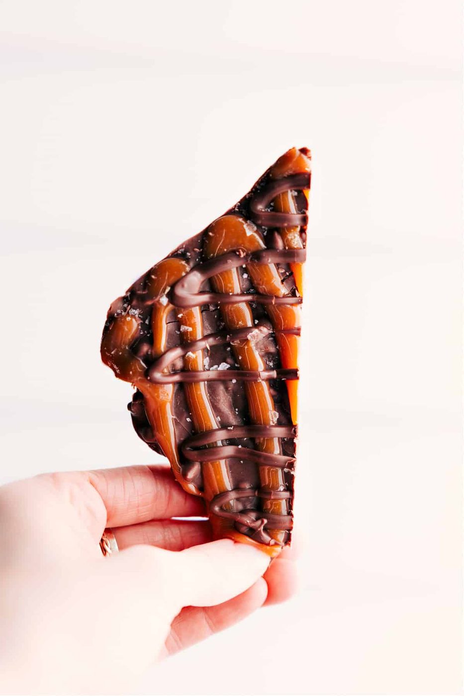 A piece of the turtle bark held up to show the lively layers of chocolate and caramel.