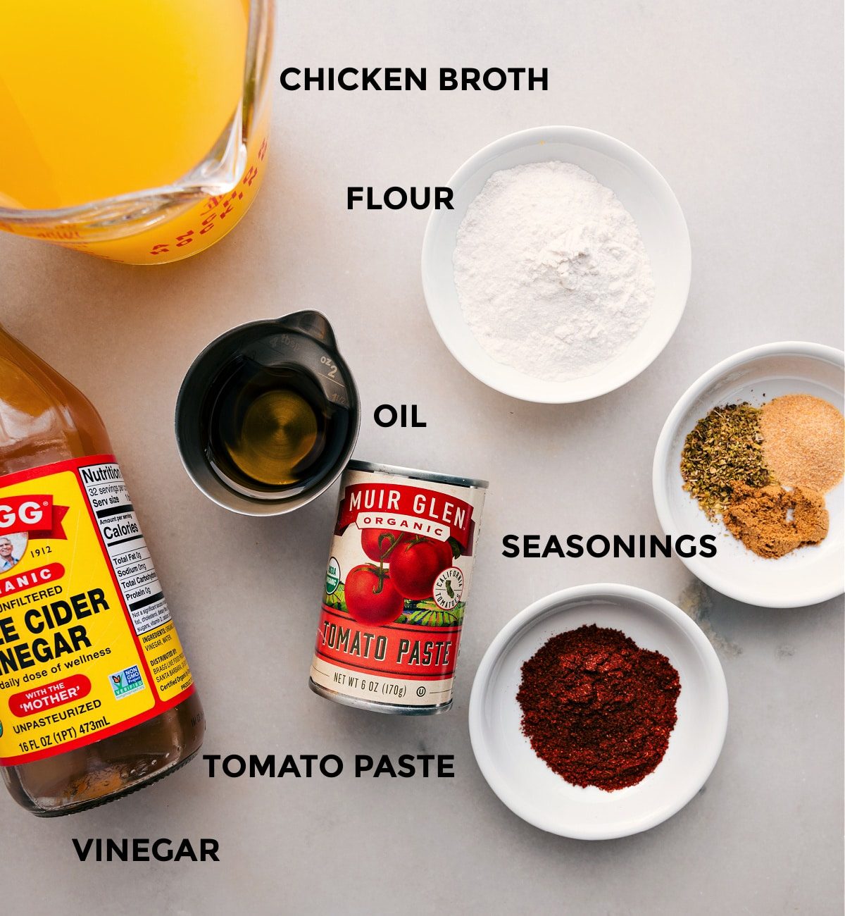 All the ingredients for this recipe are prepped and ready for straightforward assembly, including chicken broth, flour, seasonings, oil, tomato paste, and apple cider vinegar.