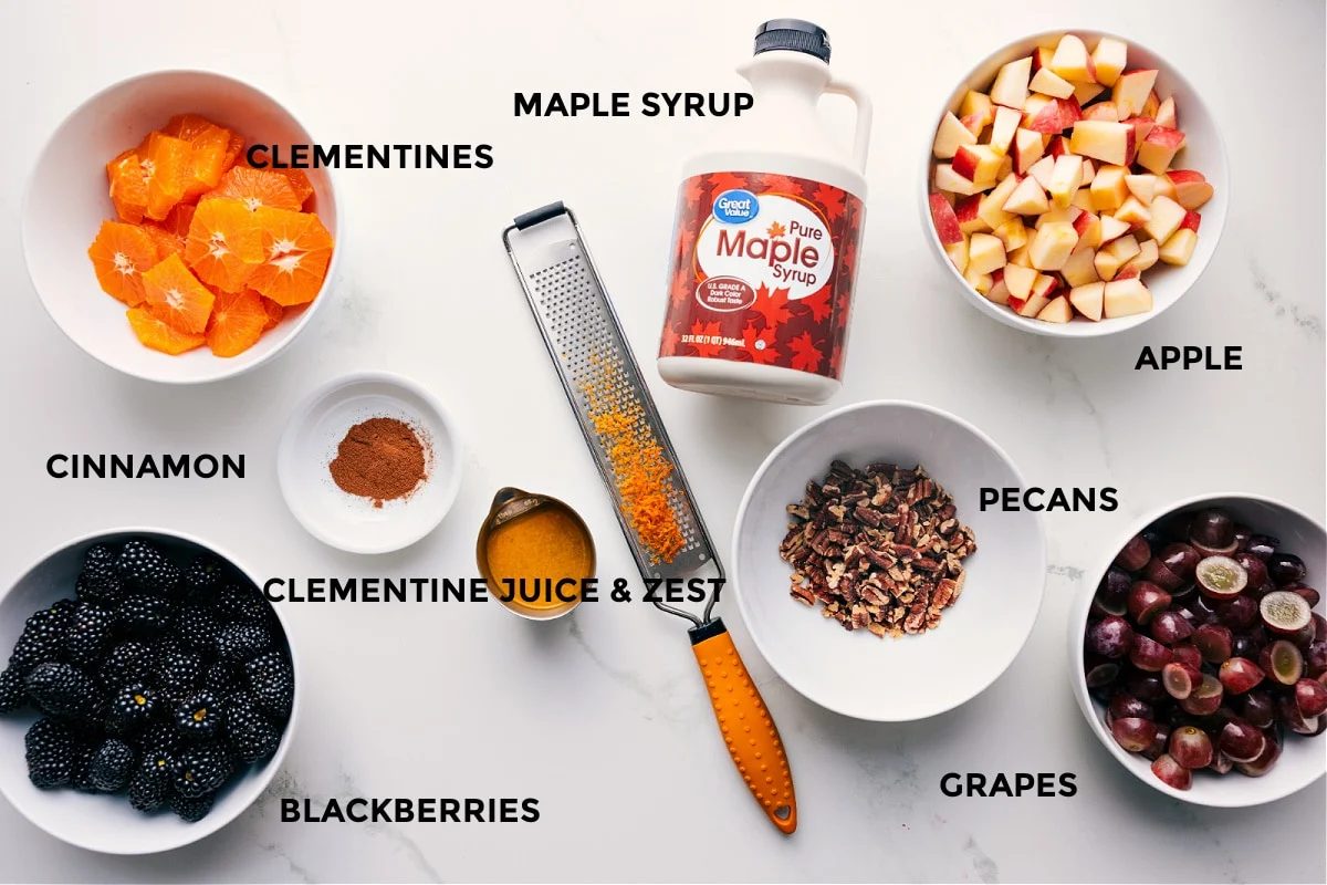All the ingredients for Fall Fruit Salad prepped for straightforward assembly, including clementines, blackberries, grapes, apples, pecans, cinnamon, orange juice and zest, and maple syrup.