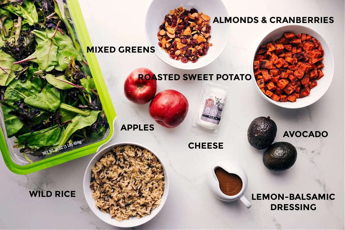 All the ingredients prepped out for straightforward assembly including mixed greens, wild rice, almonds, cranberries, roasted sweet potatoes, avocado, cheese, and dressing.