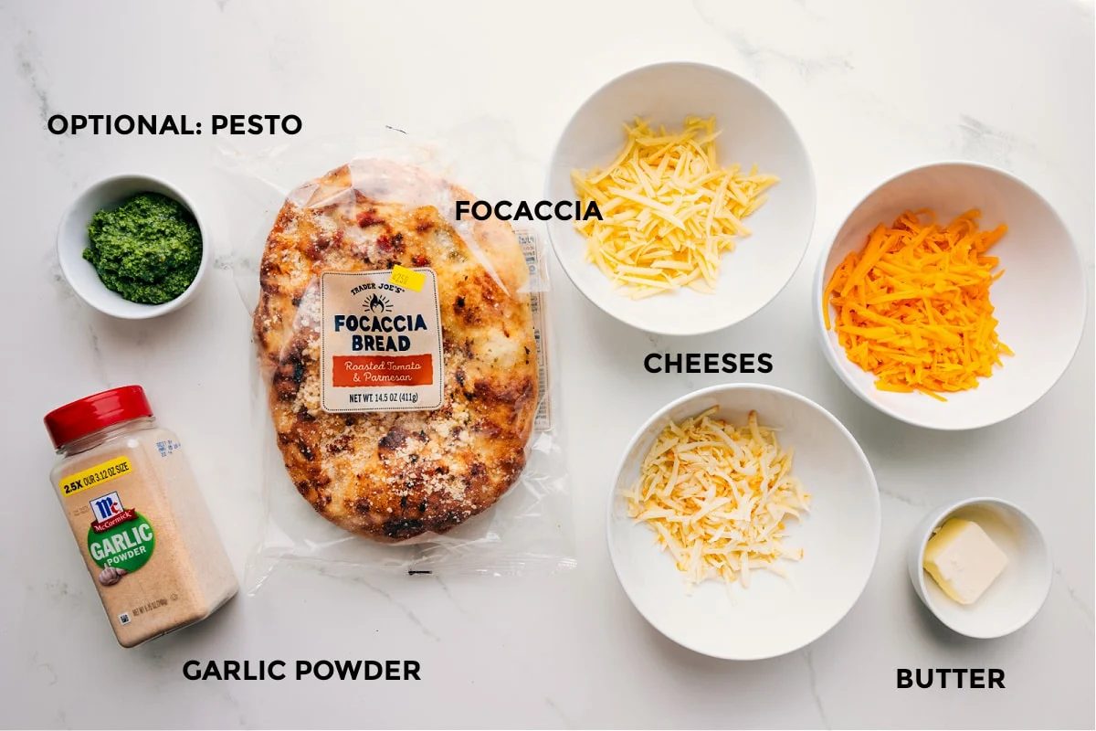 Ingredients laid out for straightforward assembly: bread, cheeses, butter, garlic powder, and skippable pesto.