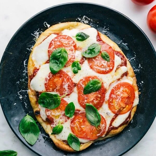 A satisfying baked naan pizza on a plate, topped with fresh basil leaves, melted cheese, and vibrant toppings.