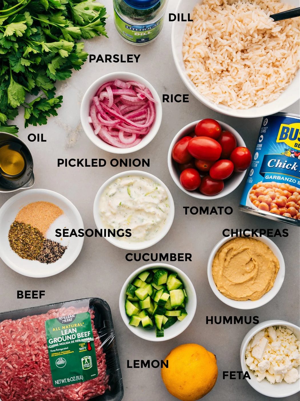 All the ingredients in this recipe are prepped for straightforward assembly: red onions, chickpeas, rice, veggies, seasonings, hummus, parsley, feta, lemon, and meat.